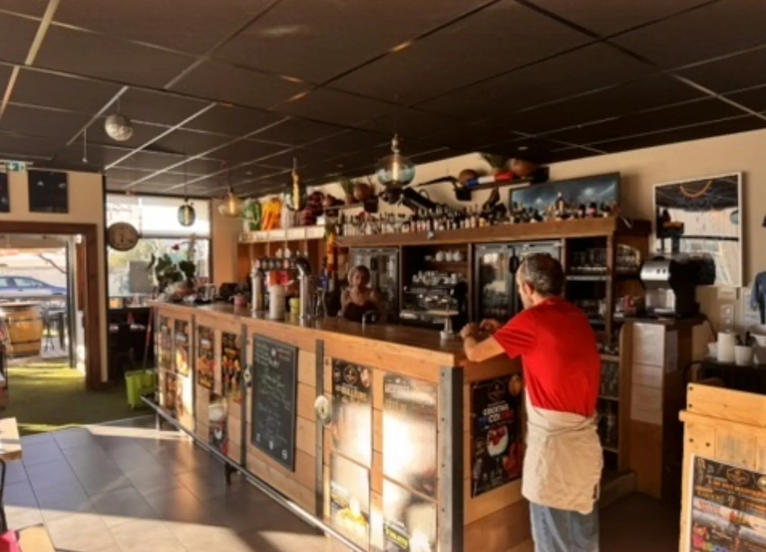 Le comptoir en bois et sa grande étagère, un membre de l’équipe accoudé