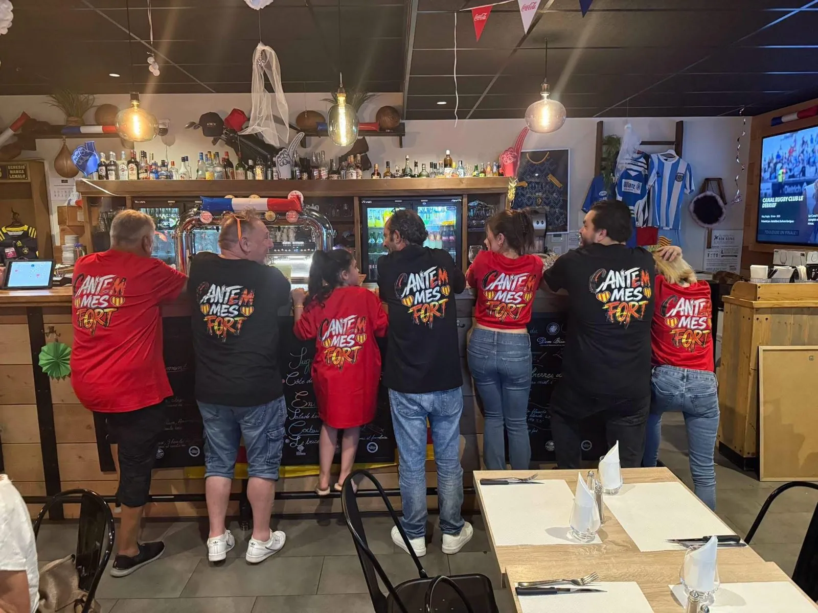 Un groupe accoudé au comptoir, en t-shirts « Cantem mes fort »