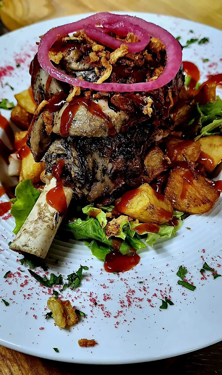 Viande sur l’os, pommes de terre rôties, salade et oignon rouge, sauce maison