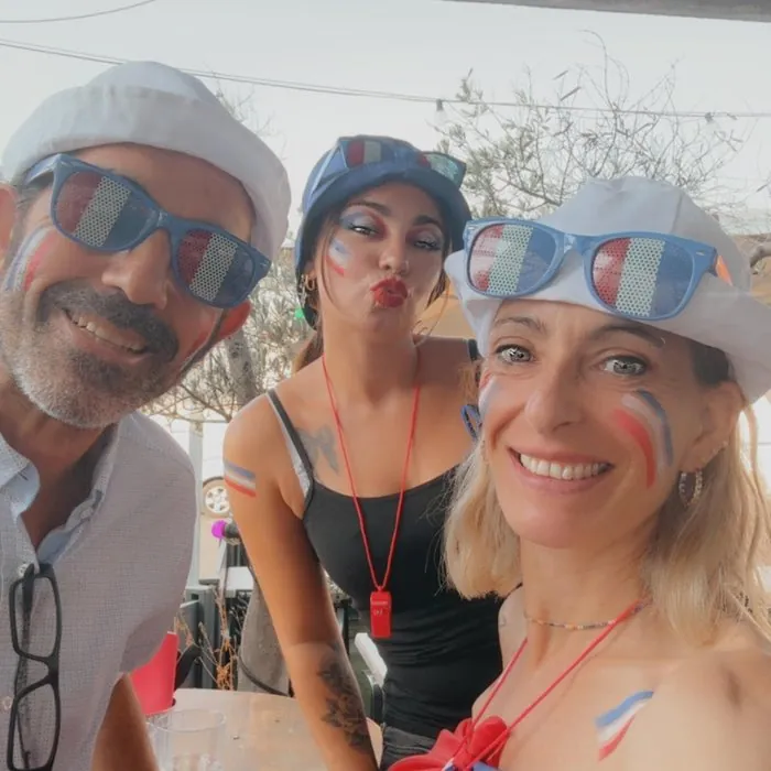 Trois clients maquillés en bleu-blanc-rouge, sous une voile d’ombrage